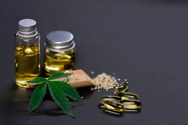 Bottles of cannabis oil, capsules, and a cannabis leaf on a dark surface