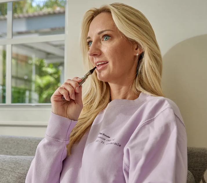 A woman sitting on a couch, holding a vape pen, contemplating.