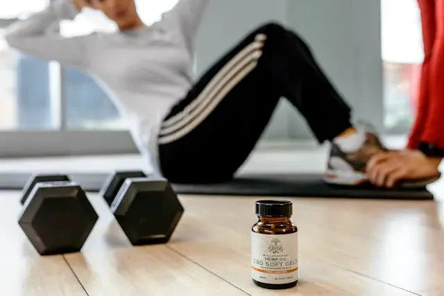 A bottle of CBD soft gel in a gym setting with dumbbells in the foreground.