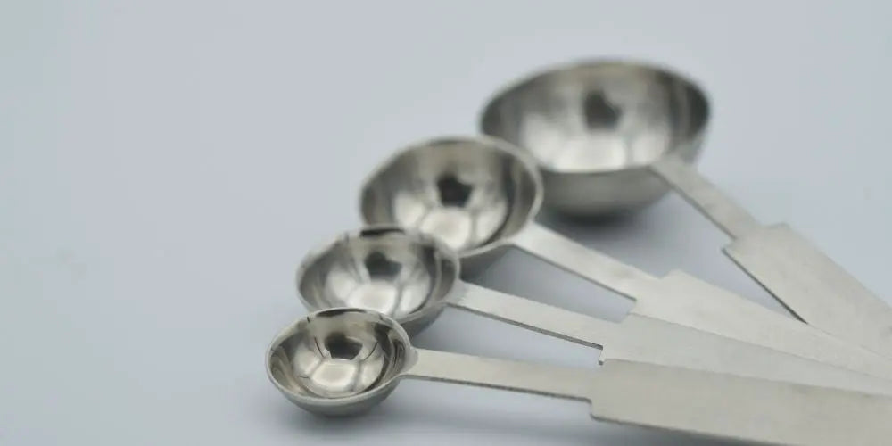 Four stainless steel measuring spoons of different sizes on a white background
