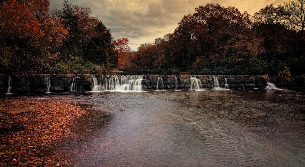 A serene landscape with a waterfall surrounded by autumn foliage.