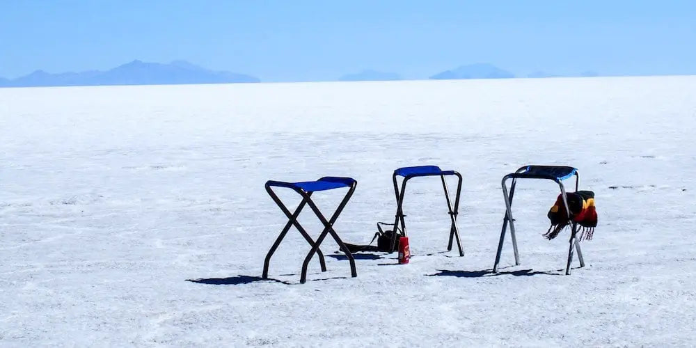 Three empty folding chairs on a salt flat under a clear blue sky.