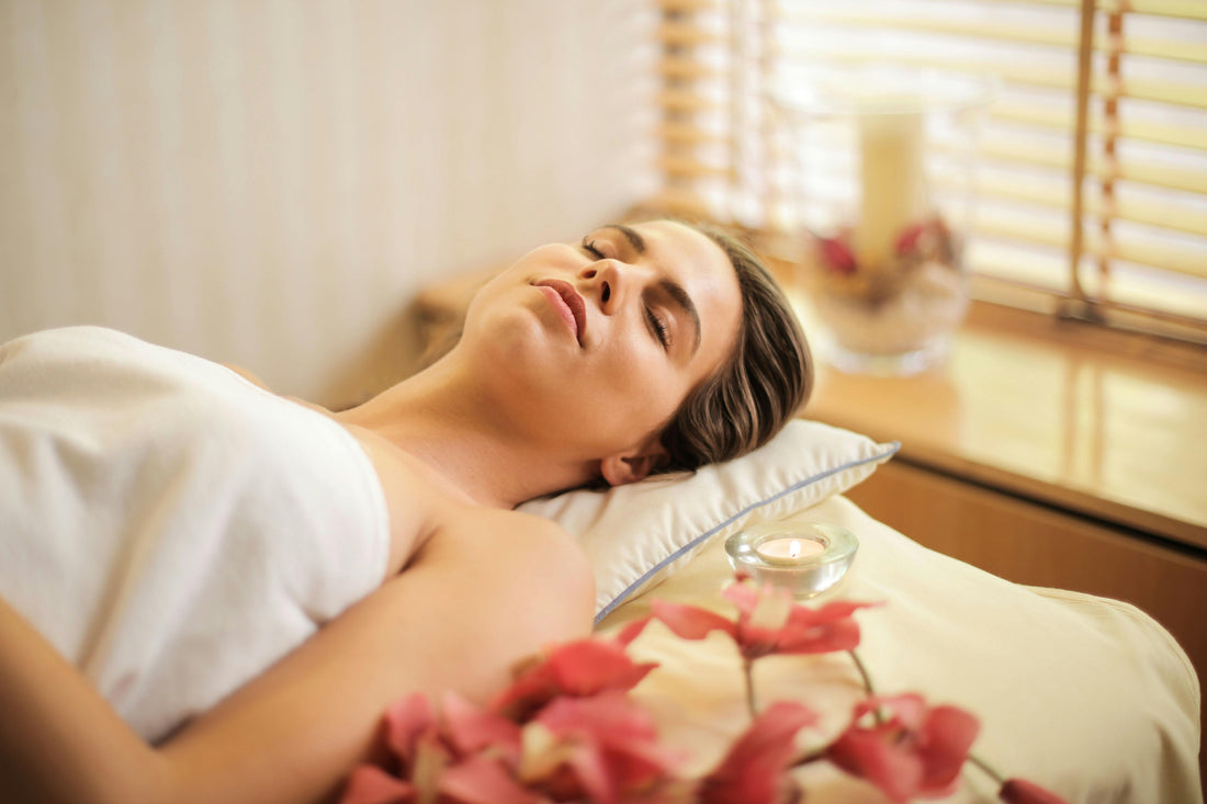 A woman relaxing on a massage table surrounded by flowers and candles.