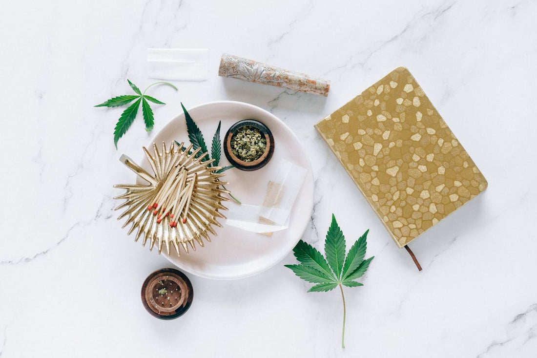 A collection of cannabis-related items including pre-rolls, a notebook, and leaves on a marble surface.