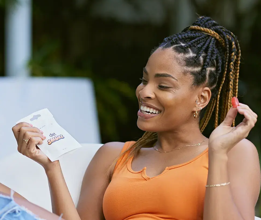 A woman smiling while holding a pack of Diet Smoke gummies.
