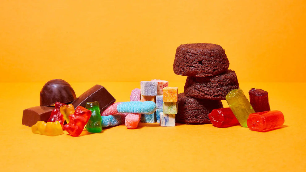 An assortment of snacks including gummies, chocolate, and brownies on a bright orange background.