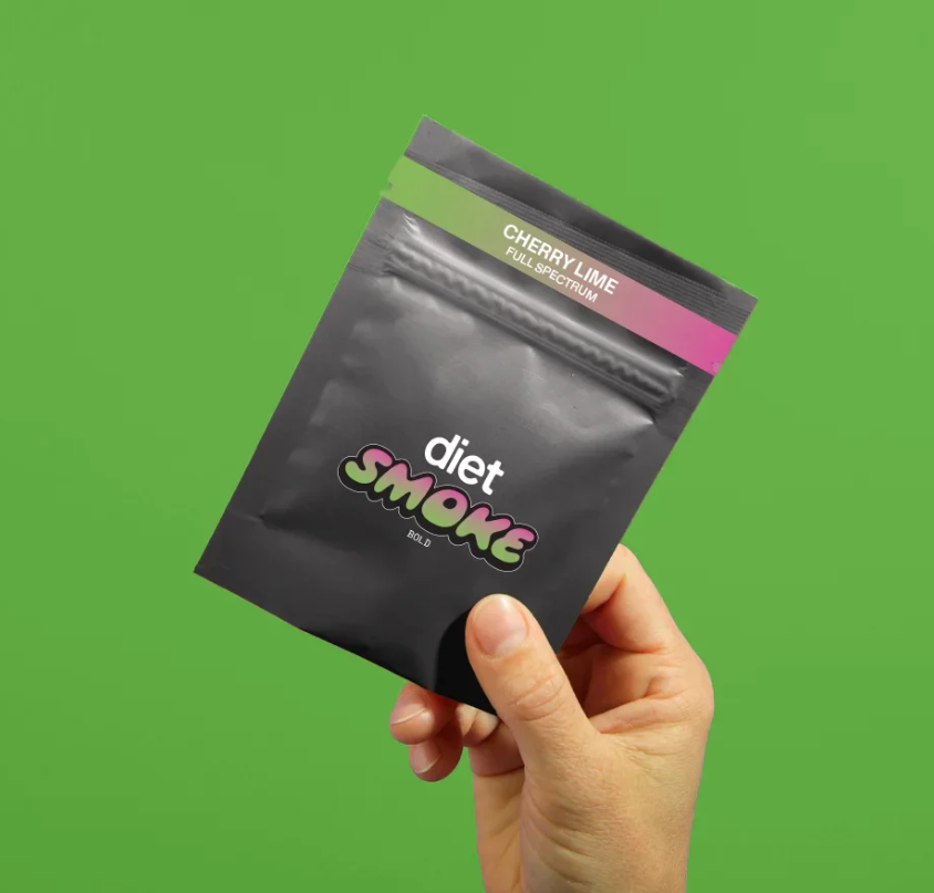Hand holding a package of Diet Smoke Cherry Lime CBD gummies on a green background