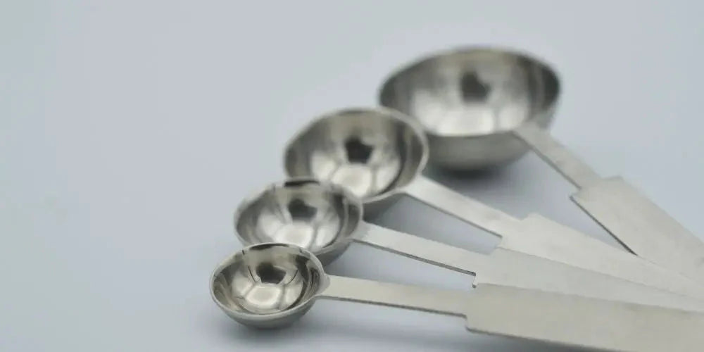 Four stainless steel measuring spoons of different sizes on a white background