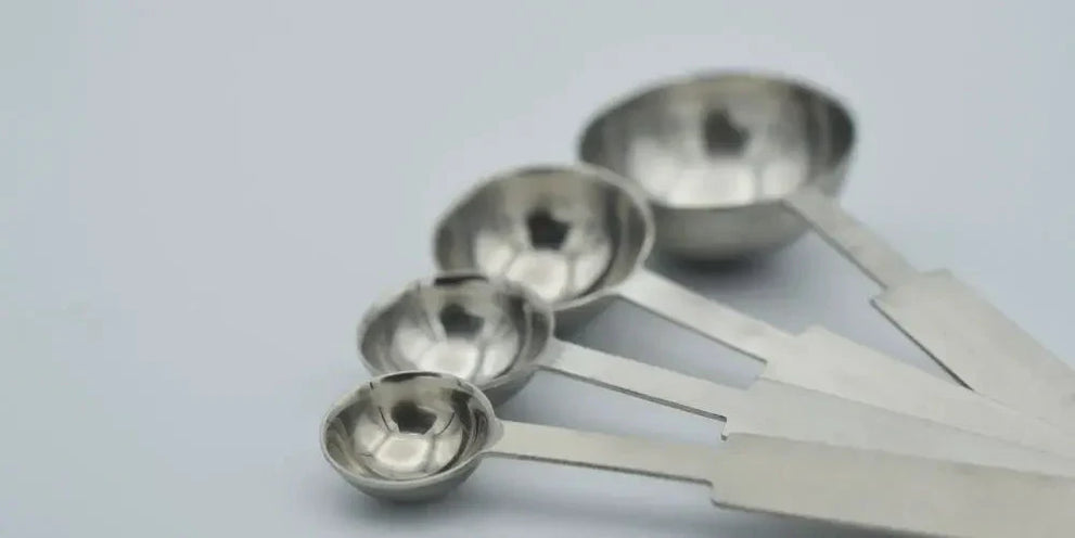 Four stainless steel measuring spoons of different sizes on a white background