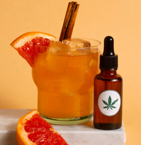 A refreshing THC drink with a slice of grapefruit and a dropper bottle on a marble surface.