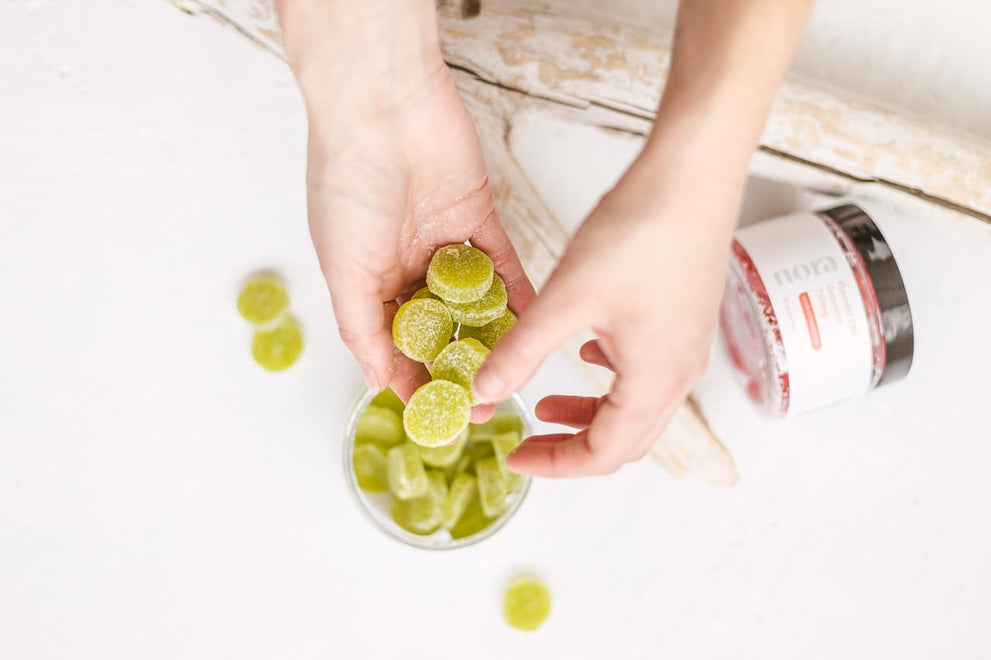 A person holding green hemp-derived gummies with a jar in the background.