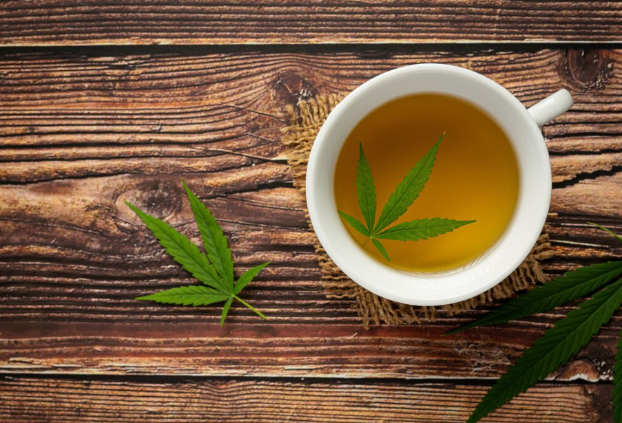 A cup of cannabis-infused tea with cannabis leaves on a wooden surface