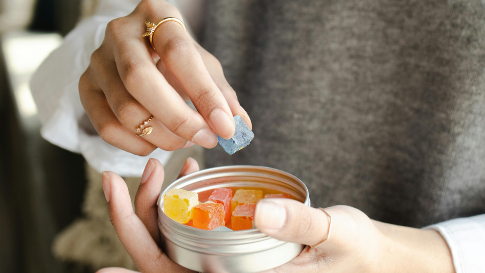 A person picking up a colorful THC gummy from a container