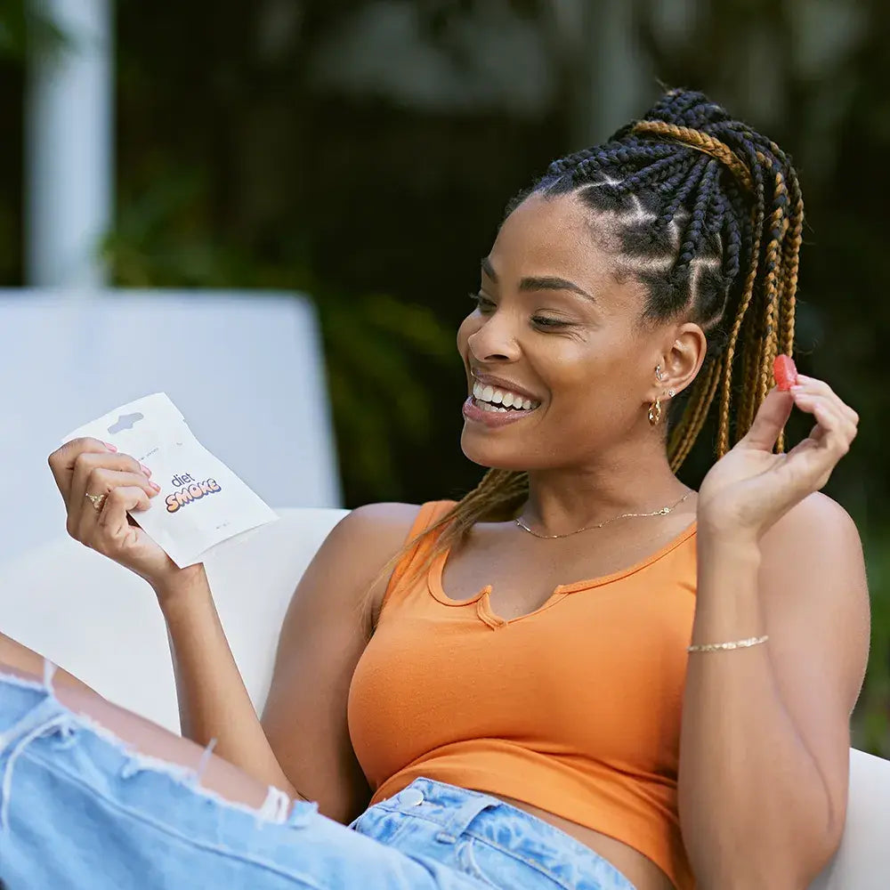 A woman holding a pack of Peach CBD Gummies while sitting outdoors, smiling.