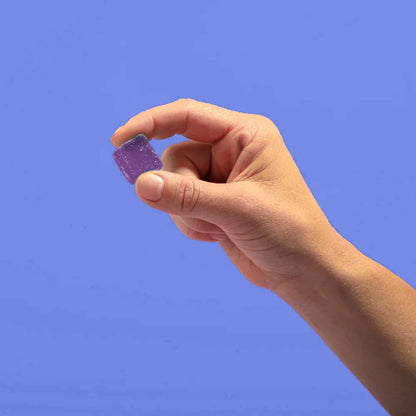 A hand holding a purple blackberry gummy against a blue background.
