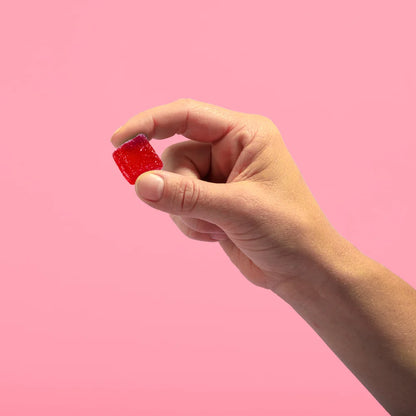 A hand holding a red gummy candy against a pink background.