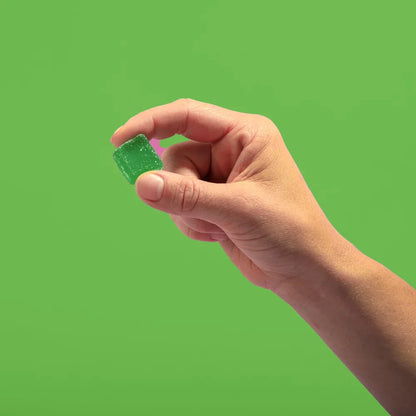 A hand holding a green cherry lime gummy against a green background.