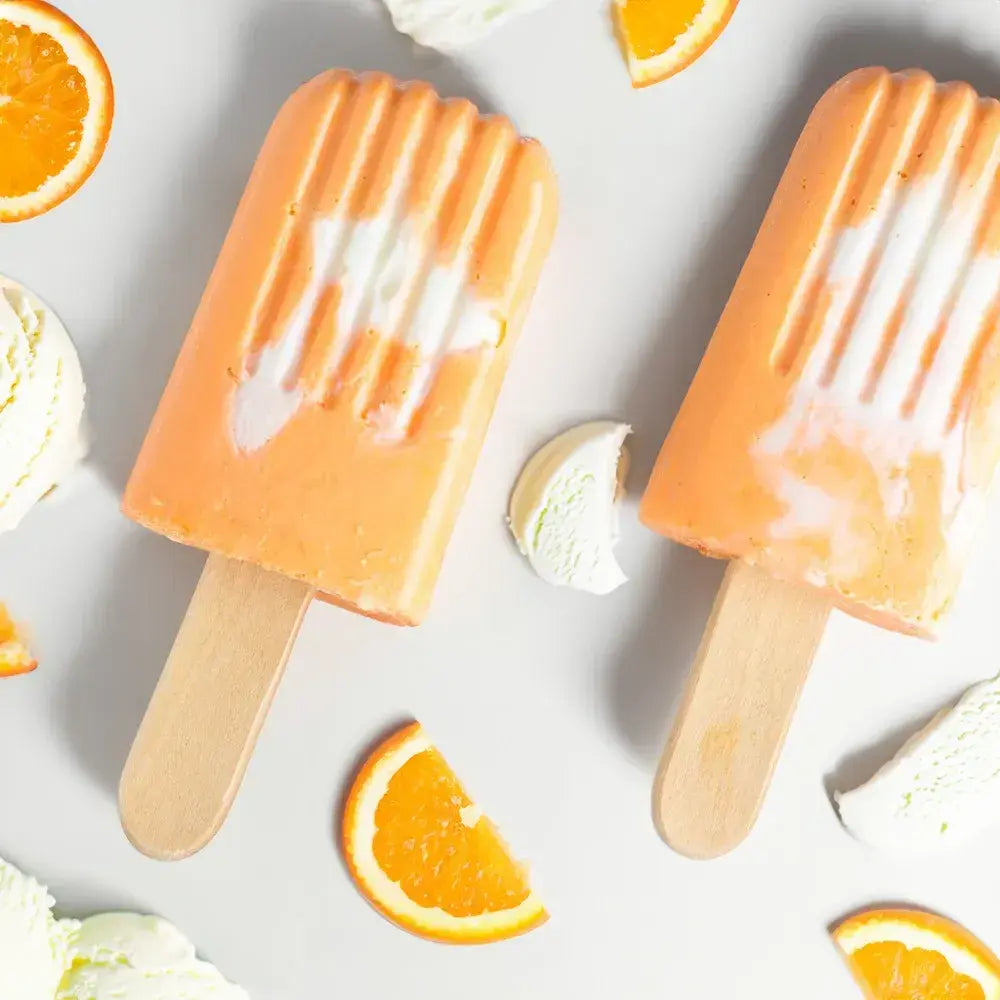 Two orange creamsicle popsicles surrounded by orange slices and ice cream