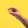 A hand holding a yellow gummy candy against a yellow background.