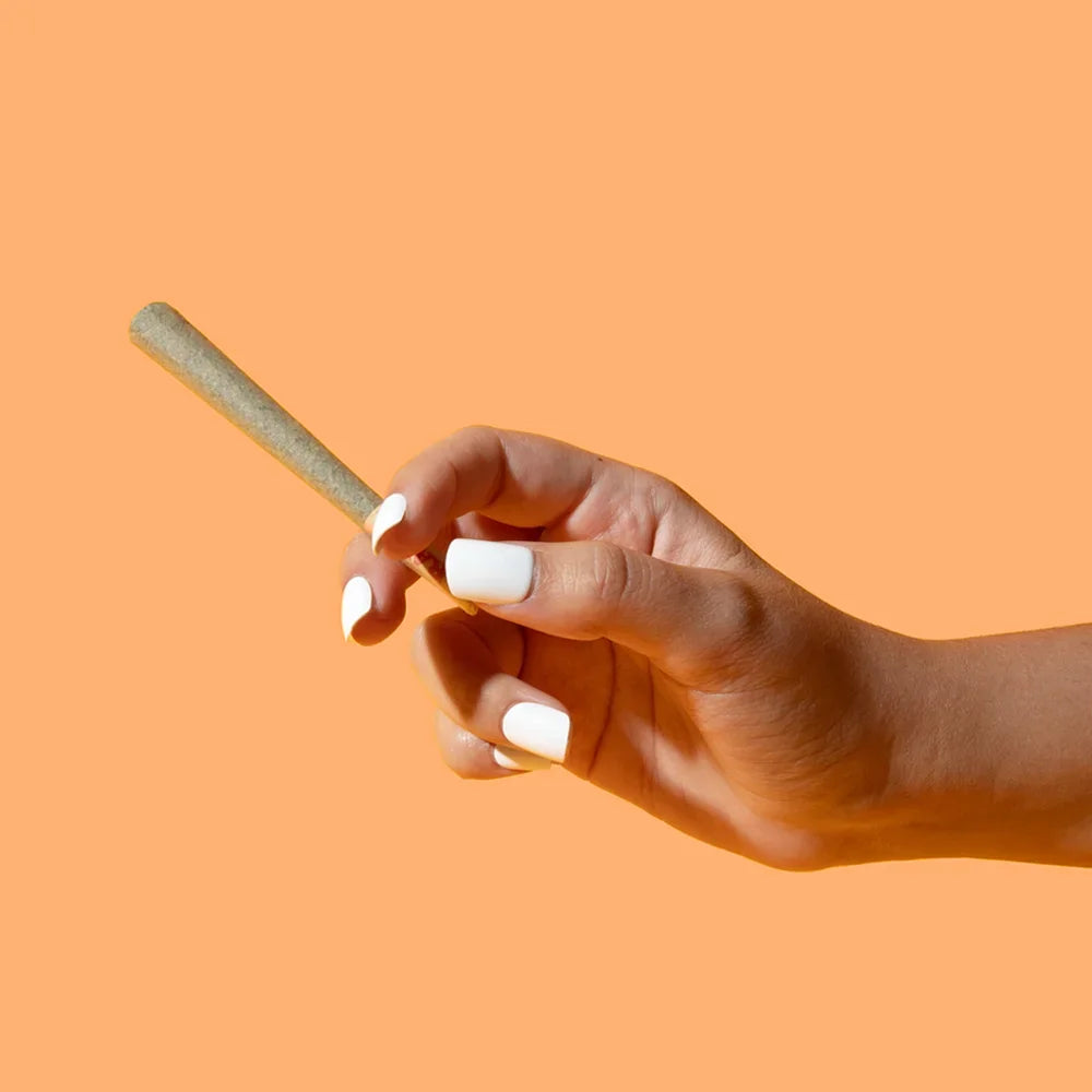 A hand holding a Tangie pre-roll against an orange background.