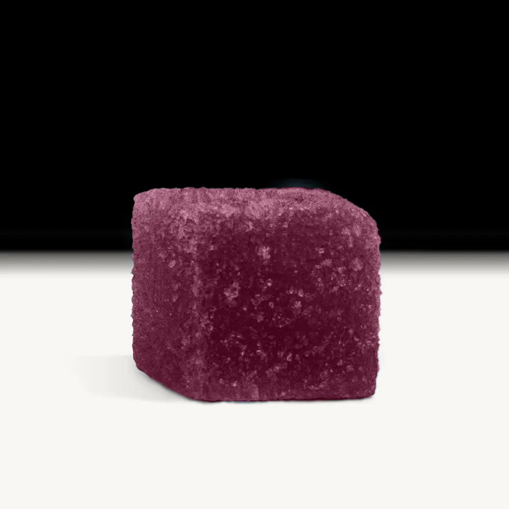 A single blackberry gummy cube on a white surface